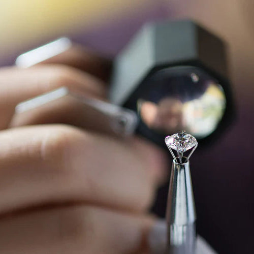 A gemologist examining a round diamond held in tweezers, with a loupe behind it