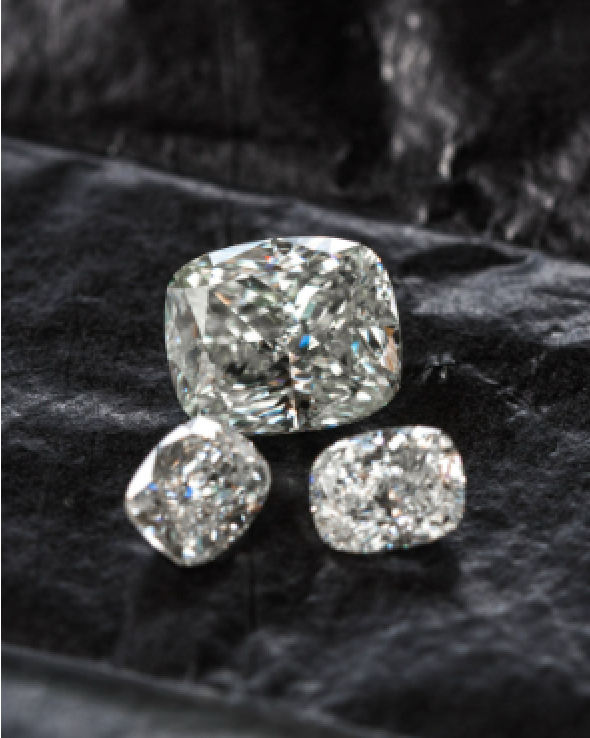 Three cushion-cut diamonds of different sizes placed side by side on dark cloth