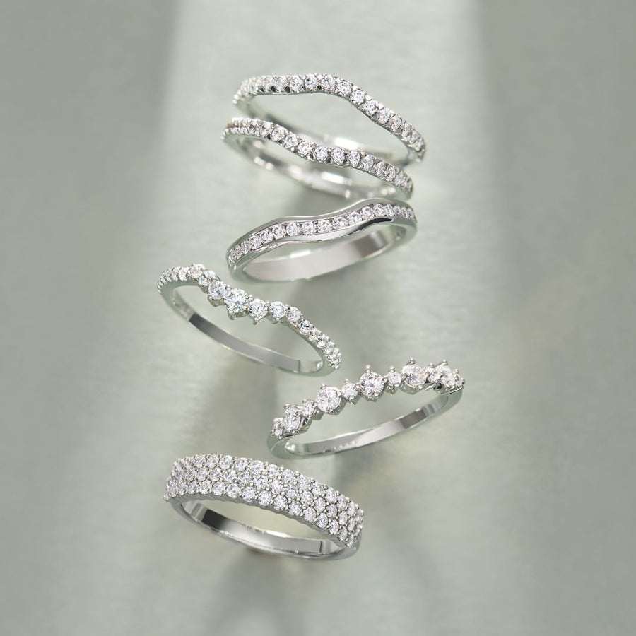 Five diamond wedding bands stacked on a soft grey surface